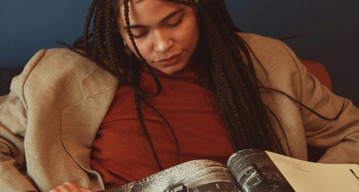 a light brown skinned Black woman with braids and a jacket reading.jpg.optimal