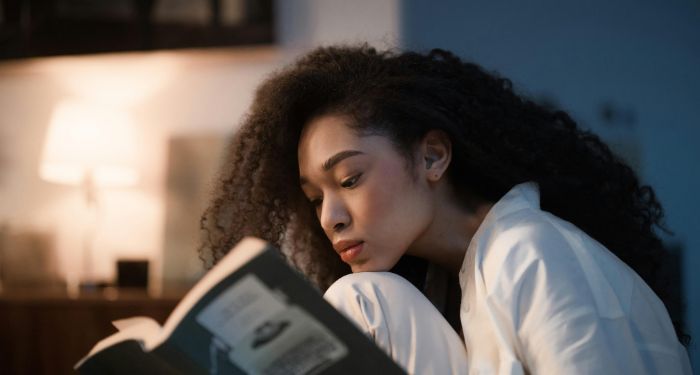 light skinned Black woman with big kinky hair reading with her chin resting on her knee.jpg.optimal