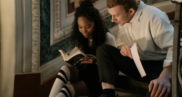 a brown skinned Black woman and a fair skinned white man sitting on stairs and reading a book.jpg.op